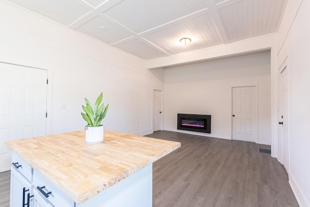 kitchen with visible vents, a center island, beamed ceiling, wood finished floors, and a glass covered fireplace