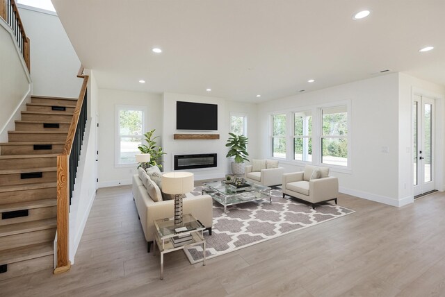living room with recessed lighting, plenty of natural light, a glass covered fireplace, and stairs