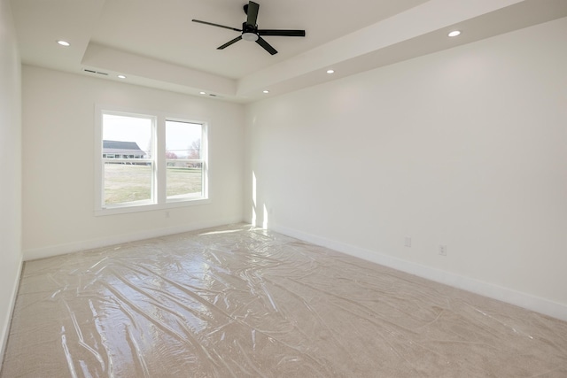 spare room featuring recessed lighting, a raised ceiling, and baseboards