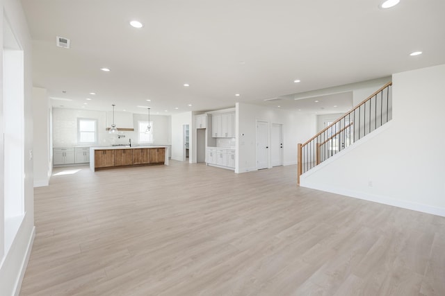 unfurnished living room featuring visible vents, baseboards, stairway, light wood-type flooring, and recessed lighting