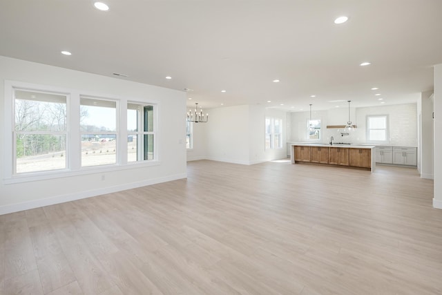 unfurnished living room with light wood-type flooring, visible vents, recessed lighting, an inviting chandelier, and baseboards