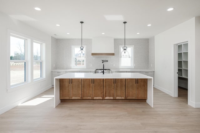 kitchen featuring light wood-style floors, tasteful backsplash, wall chimney exhaust hood, and light countertops