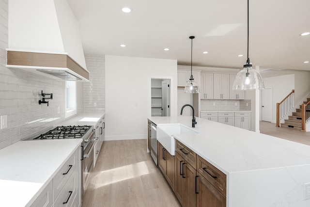 kitchen with premium range hood, light wood-style flooring, appliances with stainless steel finishes, a large island with sink, and a sink