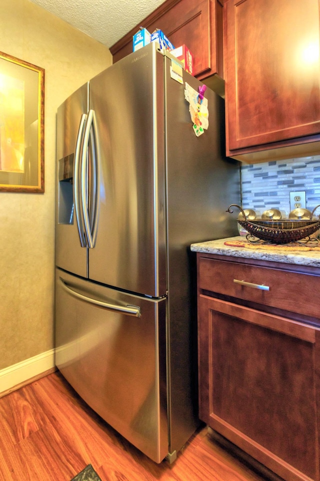 kitchen featuring decorative backsplash, stainless steel fridge with ice dispenser, light wood-style floors, and a textured ceiling