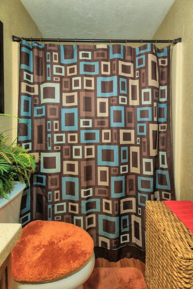 full bathroom featuring a shower with shower curtain, wood finished floors, and a textured ceiling