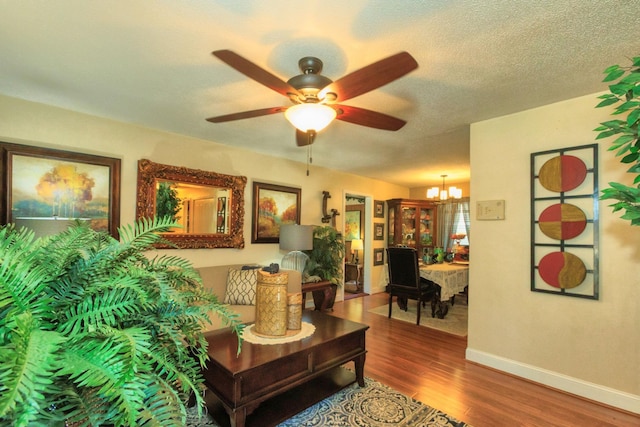 living room with ceiling fan with notable chandelier, dark wood-style floors, baseboards, and a textured ceiling