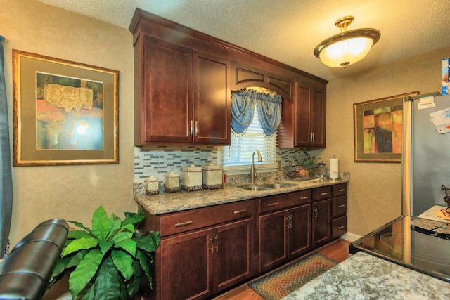 kitchen featuring tasteful backsplash, freestanding refrigerator, wood finished floors, stove, and a sink