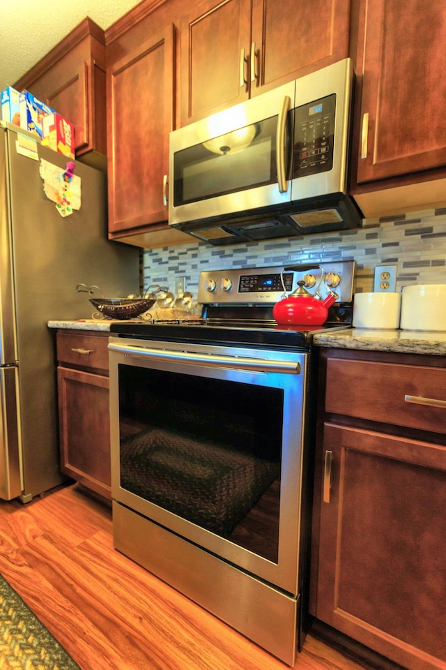 kitchen featuring stainless steel appliances, light stone countertops, tasteful backsplash, and light wood-style flooring