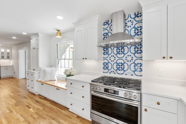 kitchen with wall chimney range hood, light wood-style floors, white cabinets, and stainless steel gas range oven