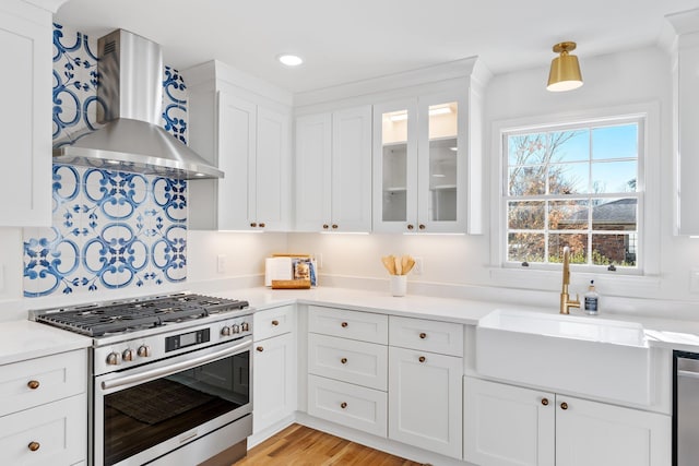 kitchen with light countertops, appliances with stainless steel finishes, white cabinetry, wall chimney exhaust hood, and a sink