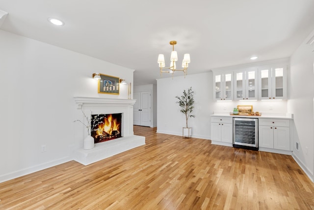 bar featuring beverage cooler, a warm lit fireplace, a bar, and light wood-style floors