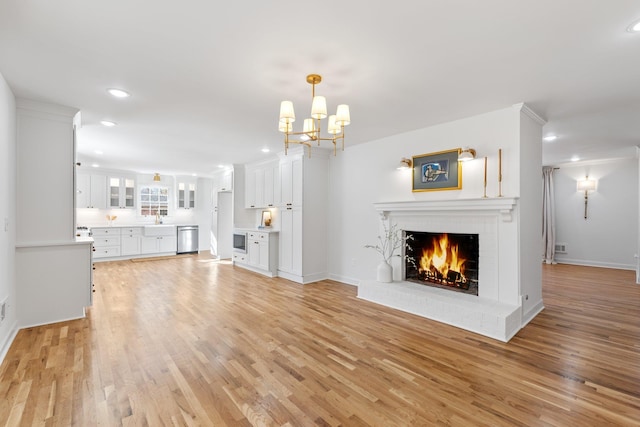 unfurnished living room featuring an inviting chandelier, a fireplace, light wood-style floors, and a sink