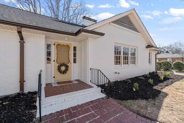 property entrance featuring brick siding and a shingled roof