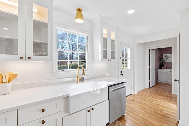 kitchen with a sink, light wood-style floors, white cabinets, glass insert cabinets, and dishwasher