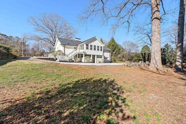 rear view of property featuring stairway, a yard, board and batten siding, and a chimney