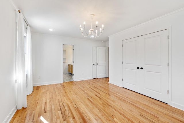 unfurnished bedroom featuring crown molding, baseboards, light wood-type flooring, ensuite bathroom, and an inviting chandelier