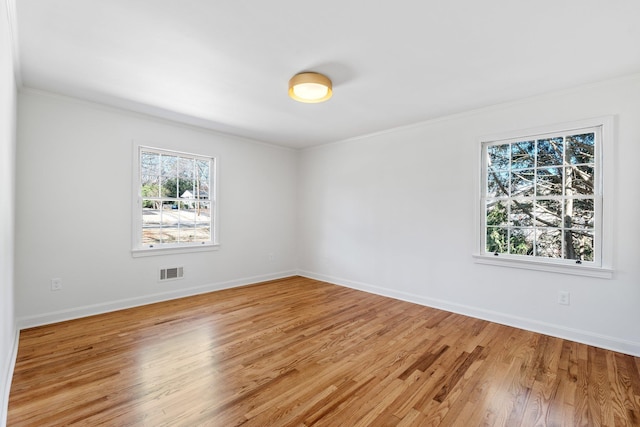 empty room featuring light wood finished floors, visible vents, and baseboards