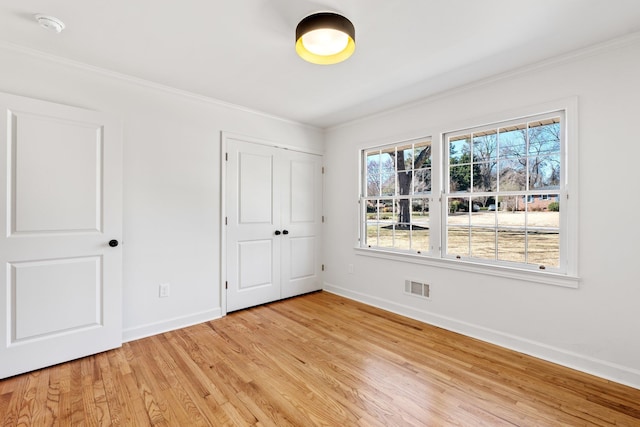 unfurnished bedroom with visible vents, baseboards, light wood-type flooring, ornamental molding, and a closet