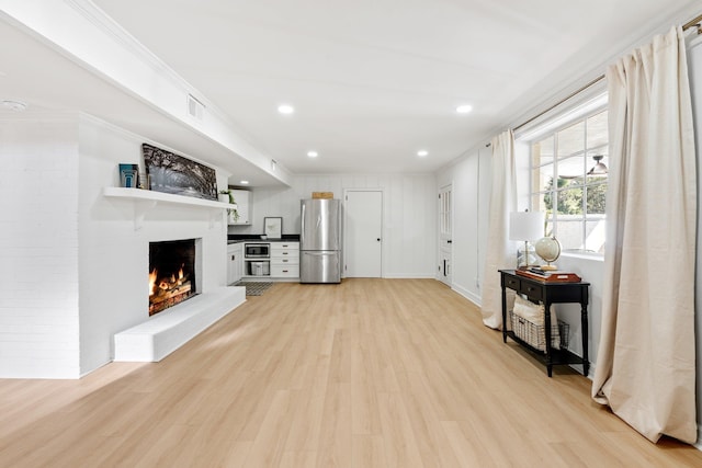 living room with light wood-type flooring, visible vents, recessed lighting, a fireplace, and crown molding