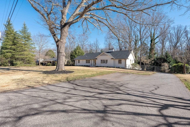 view of front of property with driveway, a chimney, a front lawn, and fence