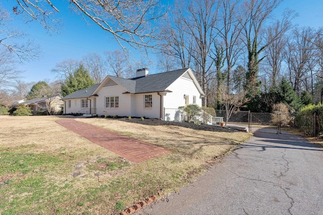 view of front facade with a gate, fence, driveway, a chimney, and a front lawn