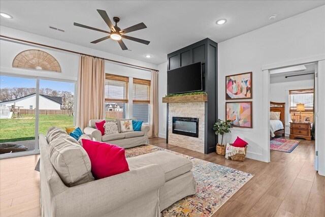 living room with a ceiling fan, visible vents, light wood finished floors, recessed lighting, and a stone fireplace