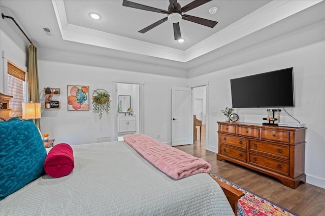 bedroom with wood finished floors, visible vents, baseboards, ensuite bathroom, and a raised ceiling