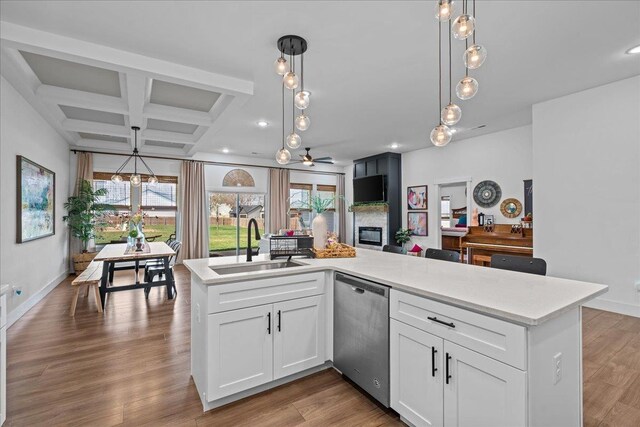 kitchen featuring light countertops, stainless steel dishwasher, wood finished floors, coffered ceiling, and a sink