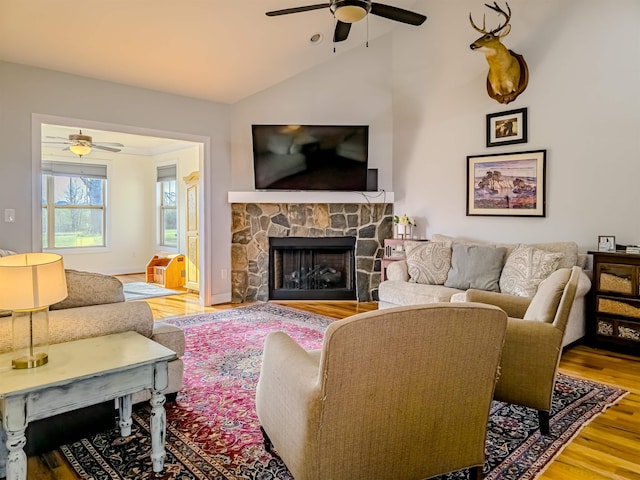 living room featuring baseboards, vaulted ceiling, a stone fireplace, wood finished floors, and a ceiling fan