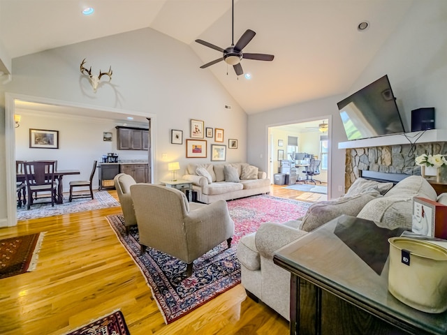 living area featuring a stone fireplace, high vaulted ceiling, light wood-style floors, and ceiling fan