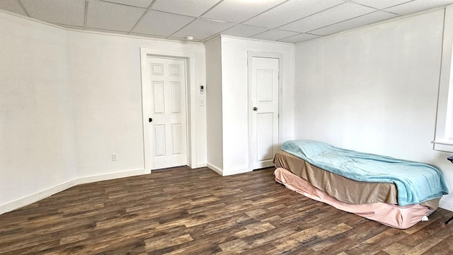bedroom featuring dark wood-style floors, a drop ceiling, and baseboards