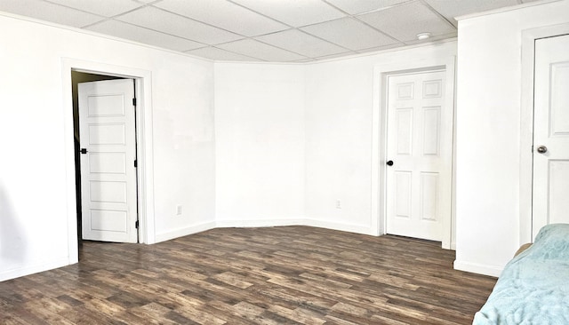 unfurnished bedroom with baseboards, a paneled ceiling, and dark wood-style flooring