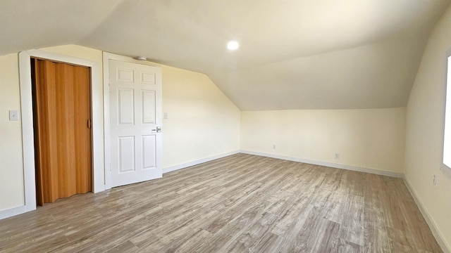 additional living space with baseboards, light wood-style floors, and vaulted ceiling