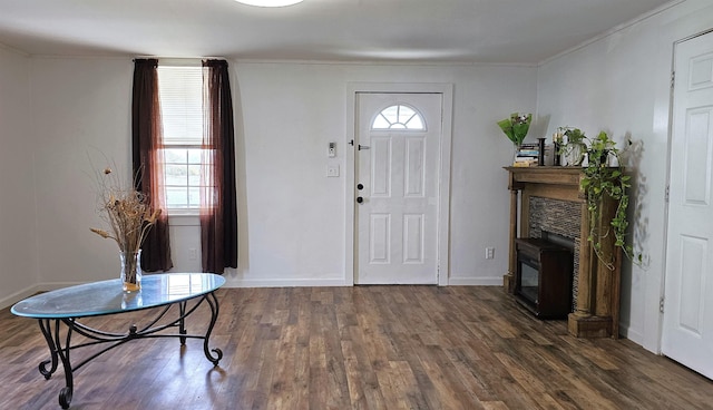 foyer entrance with a glass covered fireplace, crown molding, wood finished floors, and baseboards