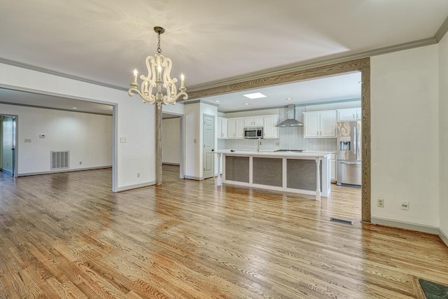 unfurnished living room with visible vents, a chandelier, crown molding, and light wood finished floors
