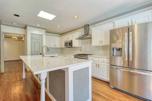 kitchen with light wood-style flooring, a sink, stainless steel appliances, white cabinets, and wall chimney range hood