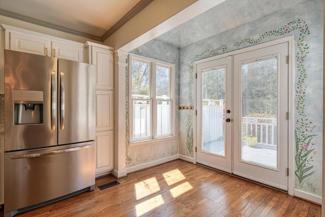 interior space with light wood-type flooring, french doors, ornamental molding, and wallpapered walls