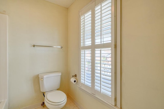 bathroom with toilet, a healthy amount of sunlight, and baseboards