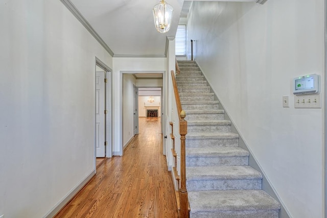 stairway with a notable chandelier, crown molding, baseboards, and wood finished floors