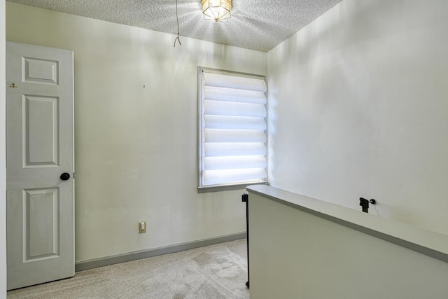 unfurnished room with light colored carpet, baseboards, and a textured ceiling