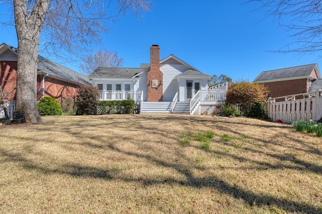 rear view of house featuring a wooden deck, a lawn, a chimney, and fence