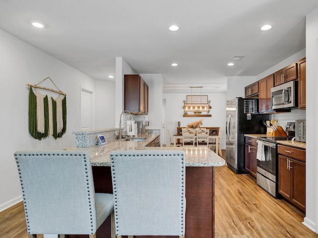 kitchen featuring light stone counters, light wood-style flooring, a peninsula, stainless steel appliances, and a sink