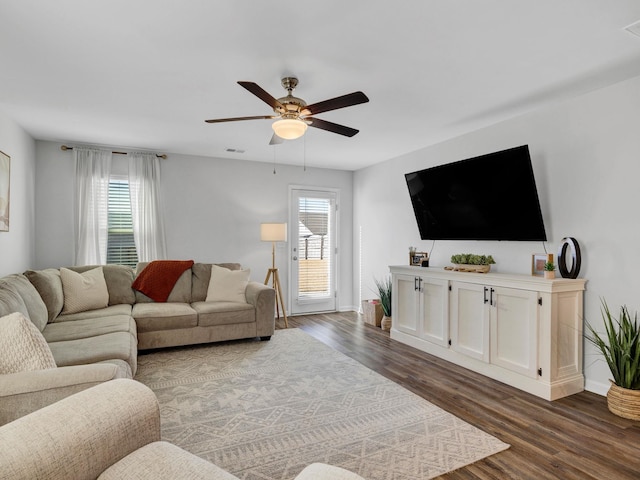 living area with visible vents, baseboards, dark wood-type flooring, and a ceiling fan