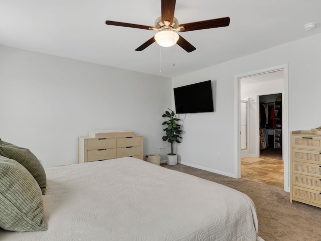 bedroom with a spacious closet, carpet, baseboards, and ceiling fan