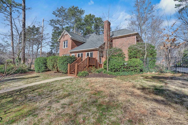 rear view of property featuring a chimney, fence, brick siding, and a yard