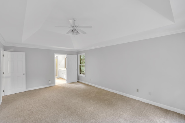 empty room with a raised ceiling, baseboards, light colored carpet, ceiling fan, and ornamental molding