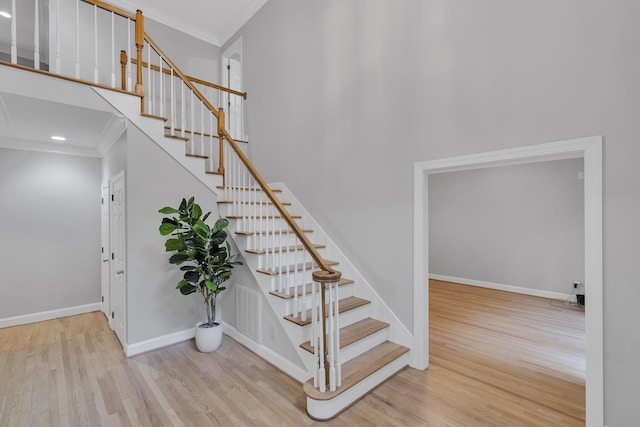 stairs with a high ceiling, crown molding, baseboards, and wood finished floors