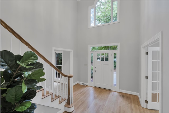 entrance foyer with stairs, visible vents, wood finished floors, and a towering ceiling