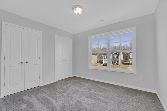 unfurnished bedroom featuring baseboards, multiple closets, visible vents, and carpet floors