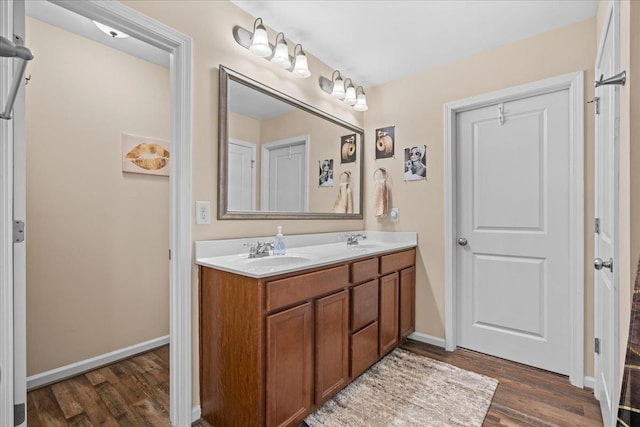 full bath with double vanity, a sink, baseboards, and wood finished floors
